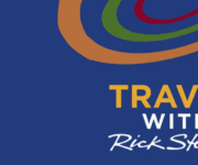 The image is a logo for the program “Travel with Rick Steves.” The background is a deep blue color. At the top, there are three curved lines in red, green, and brown, resembling stylized travel paths or trails, forming an abstract, circular pattern. Below these lines, the text “TRAVEL WITH Rick Steves” is prominently displayed. The word “TRAVEL” is in bold, uppercase yellow letters. The word “WITH” is in smaller, bold, uppercase white letters underneath “TRAVEL.” Below “WITH,” the name “Rick Steves” is written in a white, cursive font that resembles a signature. The overall design is clean and modern, with the curved lines adding a dynamic, travel-oriented feel to the logo. The text is clear and easy to read, with the deep blue background providing strong contrast.