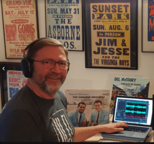 Tom Keeney in Home studio with headphones and wall of posters with couple albums